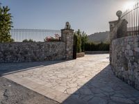 a stone fence sits near a stone building and gate in the country setting of a greek property