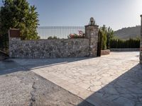 a stone fence sits near a stone building and gate in the country setting of a greek property