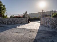 a stone fence sits near a stone building and gate in the country setting of a greek property