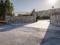 a stone fence sits near a stone building and gate in the country setting of a greek property