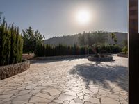 a stone fence sits near a stone building and gate in the country setting of a greek property