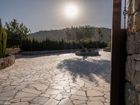 a stone fence sits near a stone building and gate in the country setting of a greek property