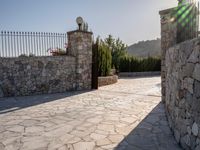 a stone fence sits near a stone building and gate in the country setting of a greek property