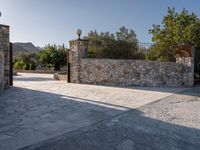 a stone fence sits near a stone building and gate in the country setting of a greek property