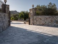 a stone fence sits near a stone building and gate in the country setting of a greek property