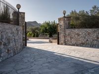 a stone fence sits near a stone building and gate in the country setting of a greek property