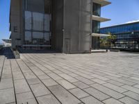 a stone floor outside of a building with buildings in the background and a bench at the end