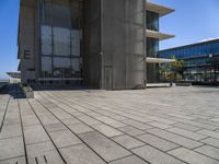 a stone floor outside of a building with buildings in the background and a bench at the end