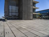 a stone floor outside of a building with buildings in the background and a bench at the end