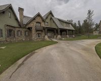 the driveway of a large stone home with two tall peaked roof dorms and a green lawn area