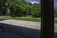 a stone path between a wooded area and trees and a park in the background with columns