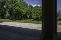 a stone path between a wooded area and trees and a park in the background with columns