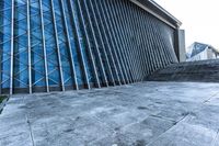 a stone pathway outside a modern building that is blue in color, looking up at the ground and sky