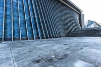 a stone pathway outside a modern building that is blue in color, looking up at the ground and sky