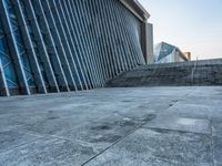 a stone pathway outside a modern building that is blue in color, looking up at the ground and sky