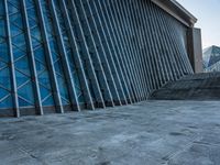 a stone pathway outside a modern building that is blue in color, looking up at the ground and sky