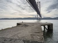 a stone pier at an island next to a large bridge with boats below the suspension span