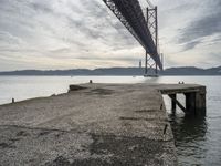 a stone pier at an island next to a large bridge with boats below the suspension span