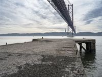 a stone pier at an island next to a large bridge with boats below the suspension span