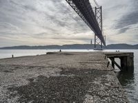 a stone pier at an island next to a large bridge with boats below the suspension span