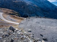 a stone road curves into the mountainside in the austrian alps, with two yellow traffic cones