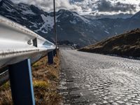 there is a metal railing on a stone road side way with mountains and hills in the background