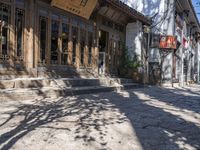 a stone street with a tree on the sidewalk and a store front with wood doors