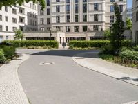 there is a stone walkway that is lined up with green plants and bushes, and a modern white building in the background