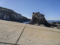 the stone walkway is leading to the beach and water's edge of a rocky coastline