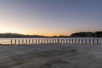 a stone walkway overlooking the sea in front of a sunset setting over the bay with mountains