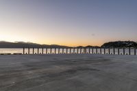 a stone walkway overlooking the sea in front of a sunset setting over the bay with mountains