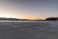 a stone walkway overlooking the sea in front of a sunset setting over the bay with mountains