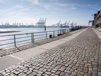a stone walkway by the water leading to a pier with many cranes on it's walls
