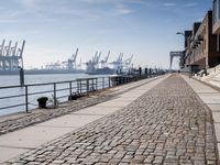 a stone walkway by the water leading to a pier with many cranes on it's walls