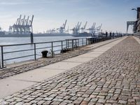 a stone walkway by the water leading to a pier with many cranes on it's walls