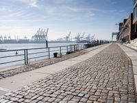 a stone walkway by the water leading to a pier with many cranes on it's walls
