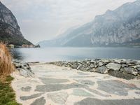 stone walkway beside the water with mountains and rocks in the background on a cloudy day