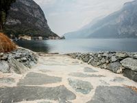 stone walkway beside the water with mountains and rocks in the background on a cloudy day