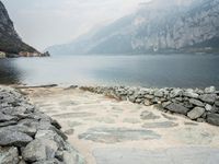 stone walkway beside the water with mountains and rocks in the background on a cloudy day