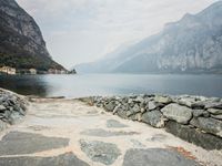 stone walkway beside the water with mountains and rocks in the background on a cloudy day