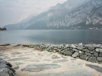 stone walkway beside the water with mountains and rocks in the background on a cloudy day