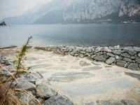 stone walkway beside the water with mountains and rocks in the background on a cloudy day