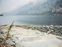 stone walkway beside the water with mountains and rocks in the background on a cloudy day