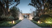 stone walkways lead to gates surrounded by trees and bushes at dusk or sunset with outdoor lighting