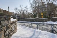 a stone wall next to the street in the snow covered area near a building and fence