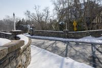 a stone wall next to the street in the snow covered area near a building and fence