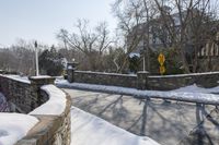 a stone wall next to the street in the snow covered area near a building and fence