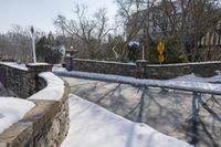 a stone wall next to the street in the snow covered area near a building and fence