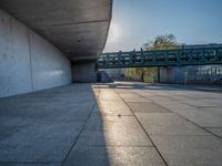 a skateboarder riding on a cement ramp next to a city street under a bridge