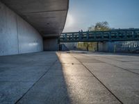 a skateboarder riding on a cement ramp next to a city street under a bridge